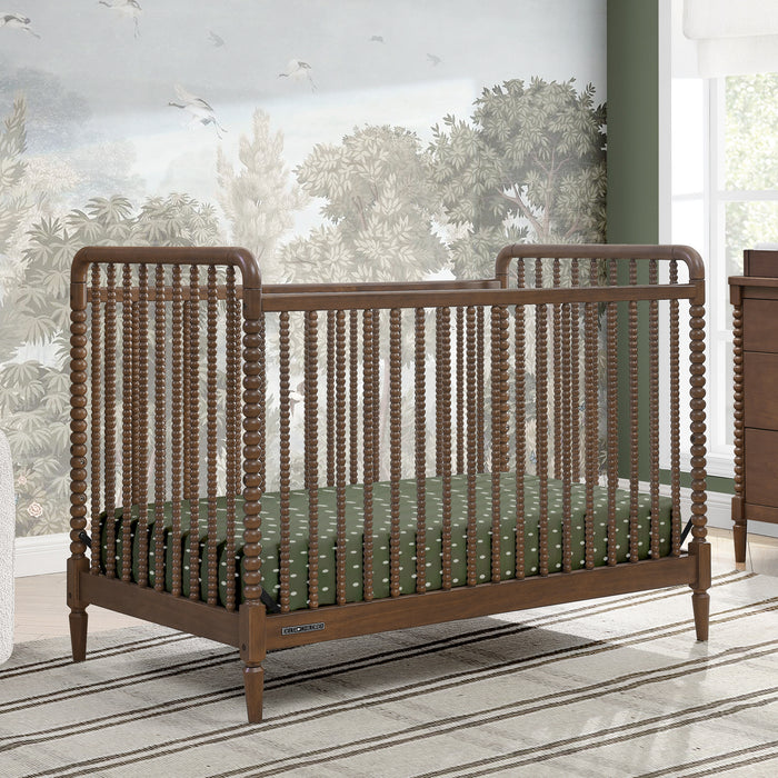 Wooden crib with green mattress in a room with large windows and greenery outside 0-Saint 4-in-1 Convertible Crib