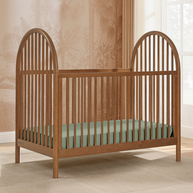 Wooden crib with a green mattress in a room with patterned wallpaper and a window. 29-Cannon 4-in-1 Convertible Crib