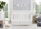 White crib in a bright nursery with decorative elements and a large window. 25-Richmond 6-in-1 Convertible Baby Crib