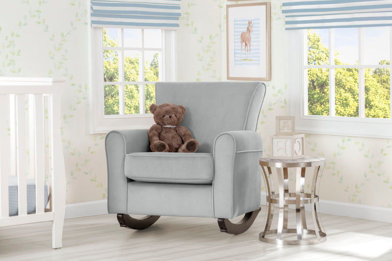 Gray armchair with a teddy bear in a nursery room with striped window blinds and a crib.