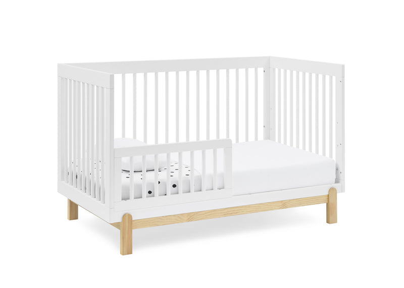A white wooden crib with a natural light oak wood base and legs, shown with a white mattress and a small white pillow on a solid white background. 13-Poppy 4-in-1 Convertible Crib