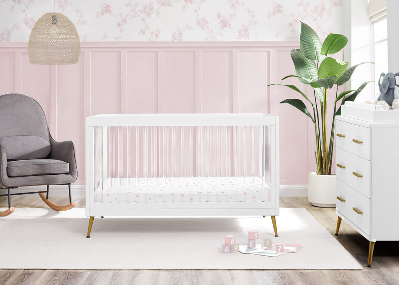Nursery room with a white crib, gray chair, and pink wall. 23-Sloane 4-in-1 Acrylic Convertible Crib