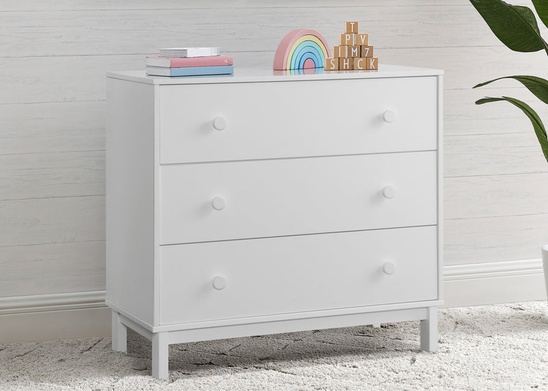 White dresser with three drawers against a light wooden paneled wall. 31-babyGap Legacy 3 Drawer Dresser with Interlocking Drawers