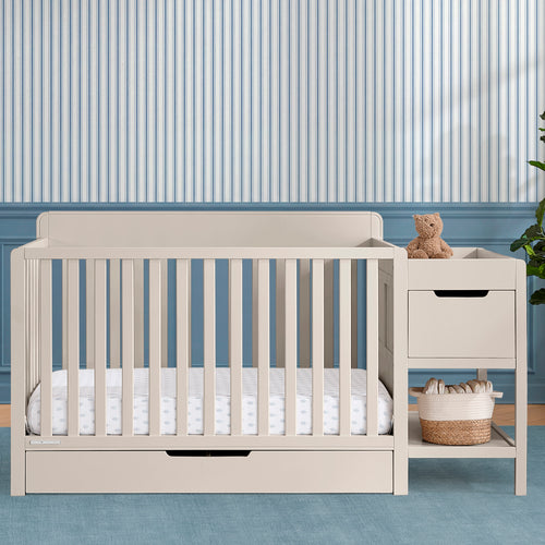 Beige crib with white bedding in a room with striped wallpaper
