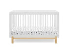A white wooden baby crib with a natural oak base and a white mattress fitted with a black polka-dot pattern, shown against a solid white background. 22-Poppy 4-in-1 Convertible Crib