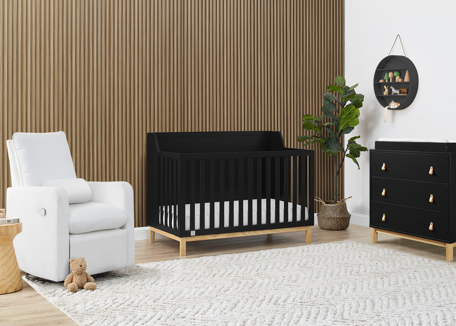 Nursery room with black crib, white armchair, and wooden dresser. 11-babyGap Oxford 6-in-1 Convertible Crib