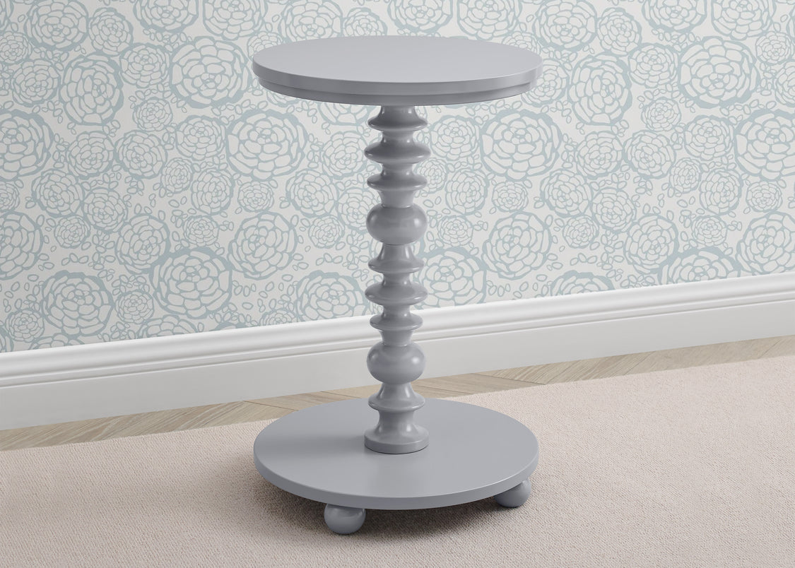 Gray side table with decorative pedestal design against a floral wallpapered wall.