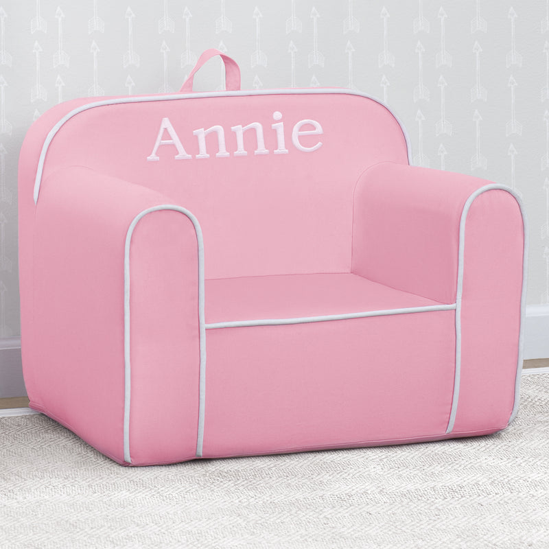 Pink children's chair with 'Annie' printed on it against a light gray wall.