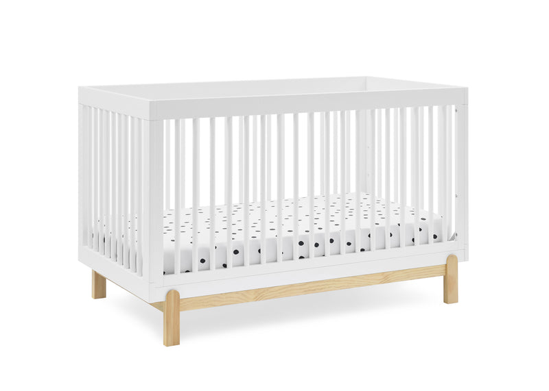 A white wooden crib with vertical slats and light natural wood legs, shown on a clean white background. A white mattress with small black polka dots is visible inside. 23-Poppy 4-in-1 Convertible Crib