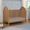 Wooden crib with white bedding in a room with floral wallpaper and a teddy bear on the floor. 32-Willa 4-in-1 Convertible Crib