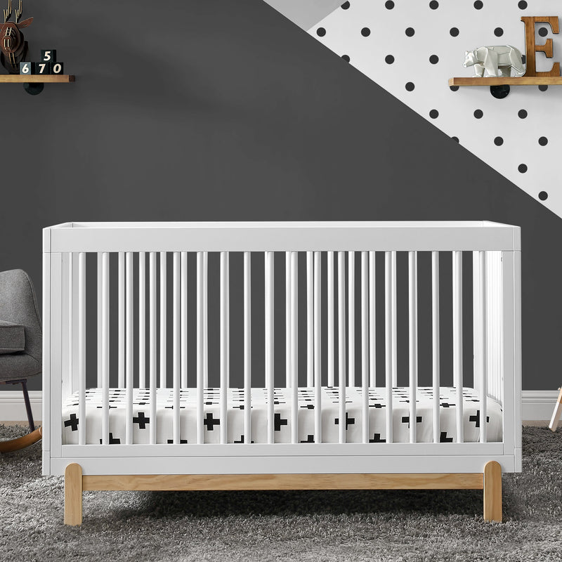 White crib in a room with a dark gray wall and polka dot pattern.