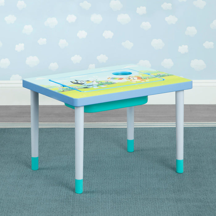 A compact sensory play table with a double-sided board and a flat top featuring Bluey artwork. The table has blue legs and a green removable plastic bin. 2-Bluey Compact Play & Learn Sensory Table