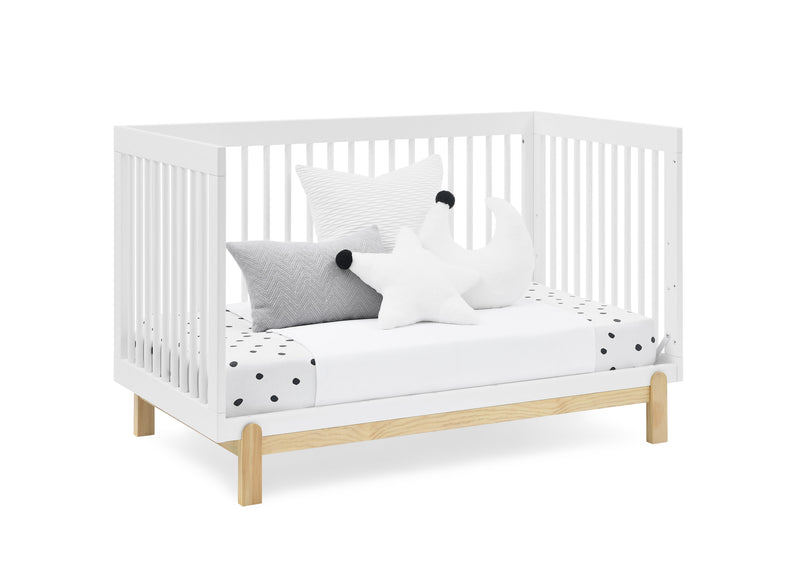 White crib with wooden legs and bedding on a white background