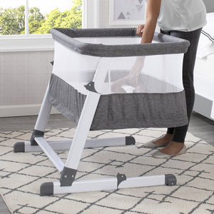 Side view of the baby bassinet with mesh sides, grey fabric, and white metal frame.