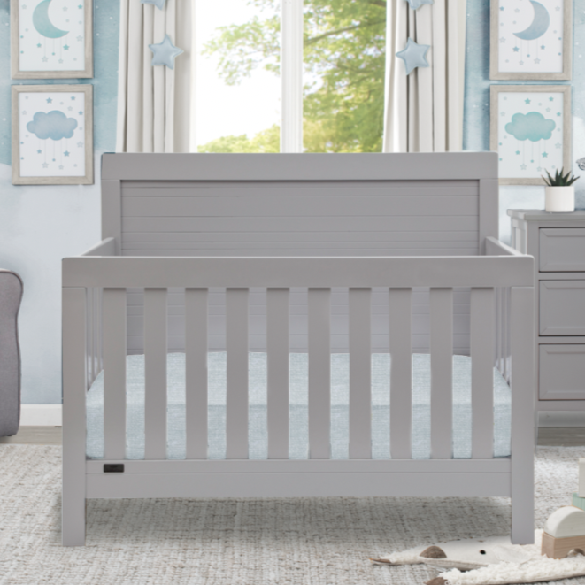 A gray Rowen 4-in-1 Crib with a mattress, positioned in a room with a window, decorative moon and stars hanging on the wall, and a gray drawer unit in the background. 1-Rowen 4-in-1 Crib